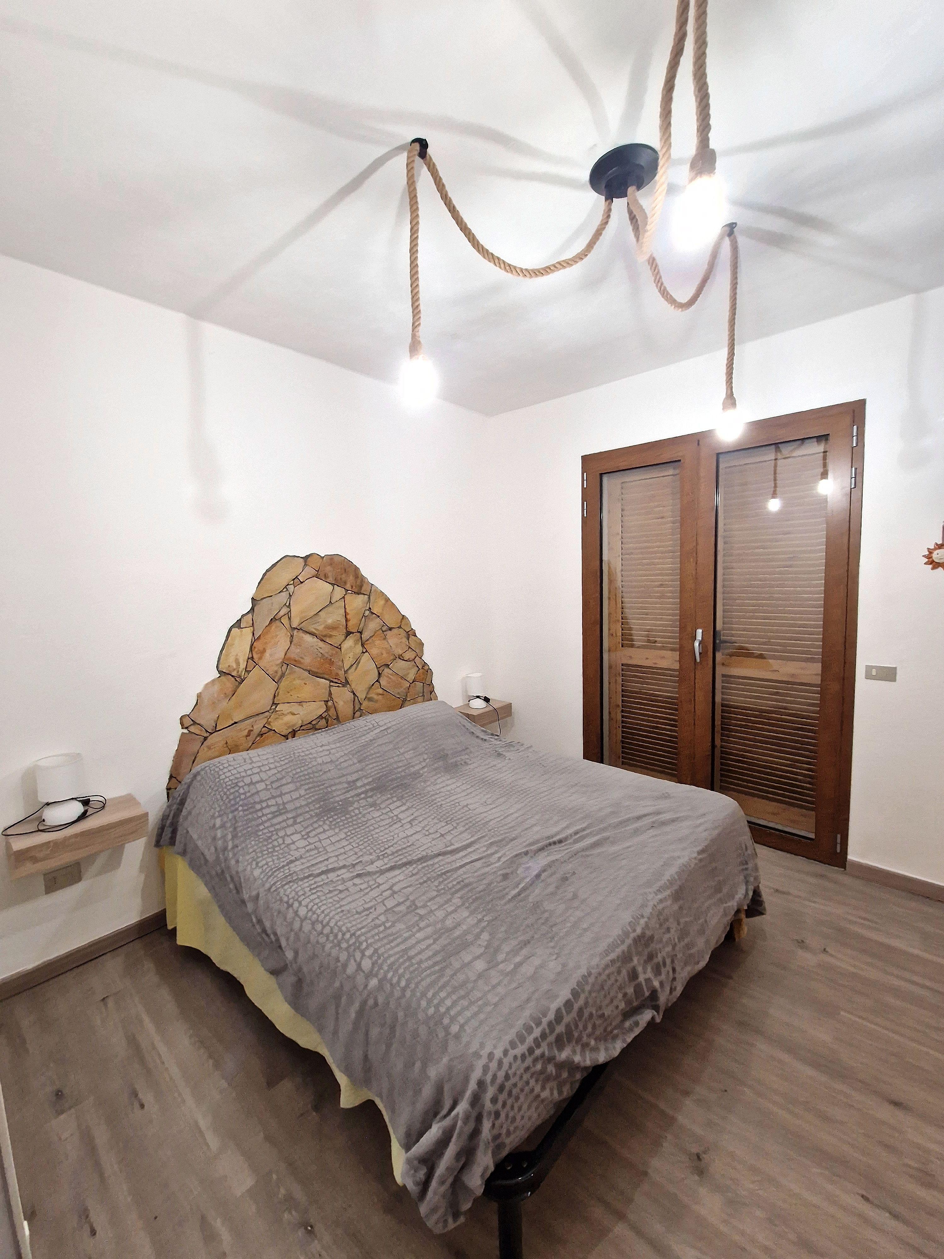 Camera da letto con testata in pietra e illuminazione a corda