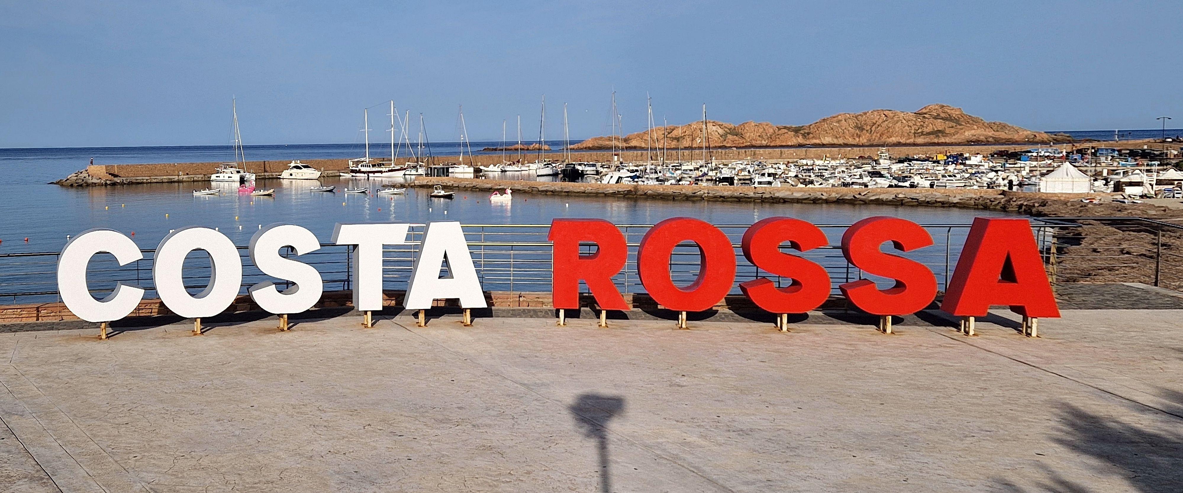 Insegna Costa Rossa con porto e barche sullo sfondo